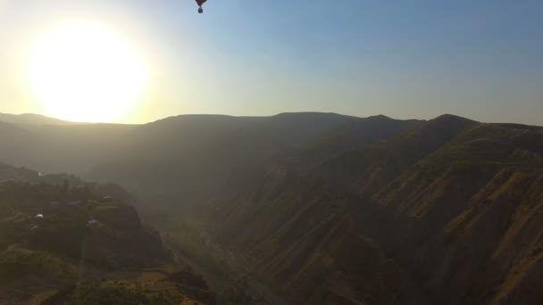 Vista del globo aerostático volando sobre el valle de la montaña y el pueblo armenio, puesta de sol — Vídeo de stock