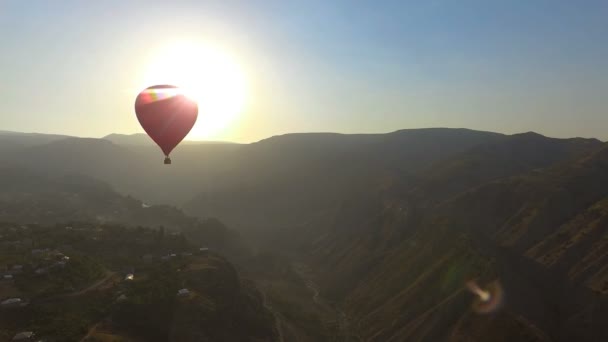 Вид с воздуха на воздушный шар, летящий над горной деревней на красивом закате — стоковое видео