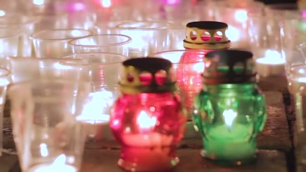 Крупный план нескольких мемориальных свечей, горящих ночью в разных цветах — стоковое видео