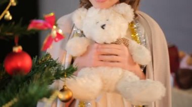 Süslü çam ağacının yanında duran ve oyuncak ayı tutan küçük kız Close-Up