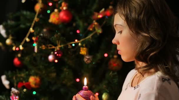 Ребенок задувает украшенную рождественскую свечу и загадывает желание, волшебные моменты — стоковое видео