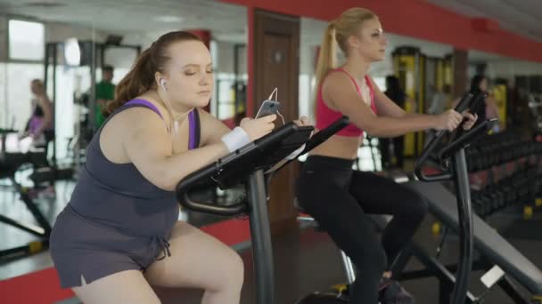 Femme en surpoids paresseux chevauchant lentement à vélo d'exercice et défilant sur le téléphone — Video