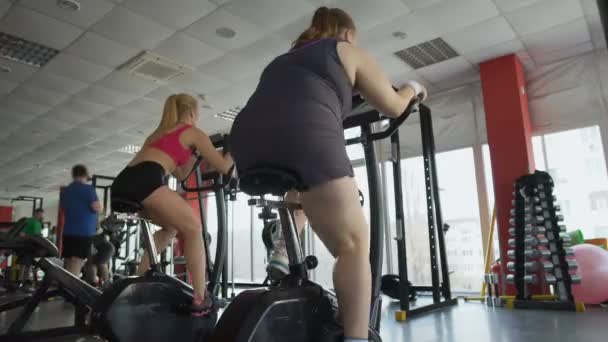 Mujer obesa trabajando en cuerpo sano en gimnasio, mujer regordeta montando una bicicleta estática — Vídeo de stock