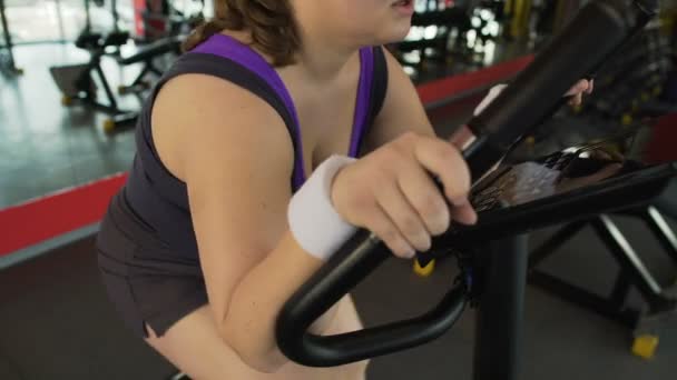 Κίνητρα παχύσαρκη γυναίκα εργάζεται σκληρά στο στατικό ποδήλατο στο γυμναστήριο, απώλεια βάρους — Αρχείο Βίντεο
