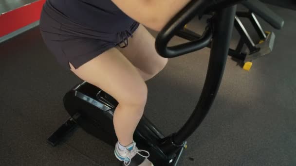 Obese woman pedaling on stationary bike in the sports club, weight loss workout — Stock Video