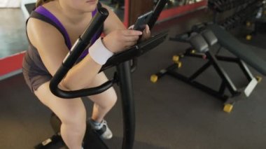 Yavaş yavaş sabit Bisiklet pedal ve telefon üzerinde kaydırma tembel şişman kadın