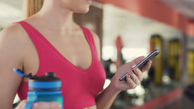 Fitness uygulama, sağlıklı kadın binicilik egzersiz bisikleti sırasında telefonda kaydırma