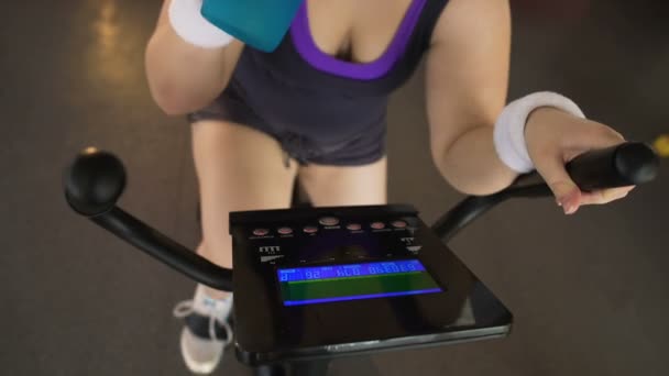 Obez kadın bir egzersiz bisikleti ve içme suyu, fitness ve Sağlık at binme — Stok video