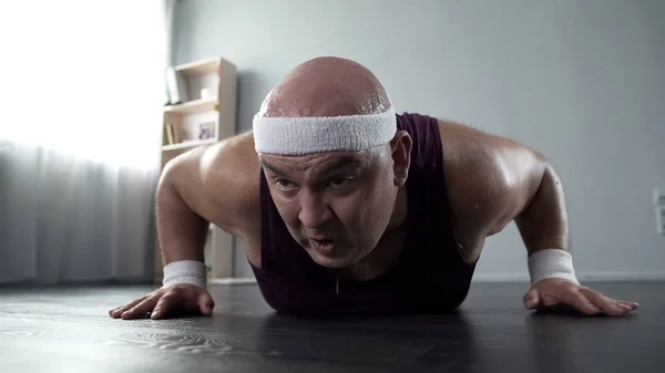 Потный мужчина со слабыми мышцами рук пытается сделать отжимания дома, тренировки — стоковое фото