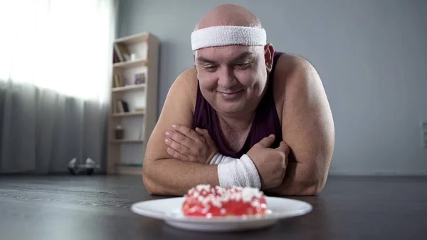 滑稽肥胖的人躺在地板上, 看着甜甜圈的爱, 毅力 — 图库照片