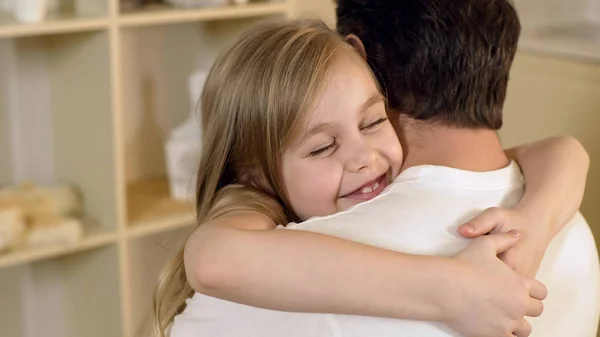 Mooie kleine meisje knuffelen vader zachtjes met een tevreden glimlach op het gezicht, familie — Stockfoto