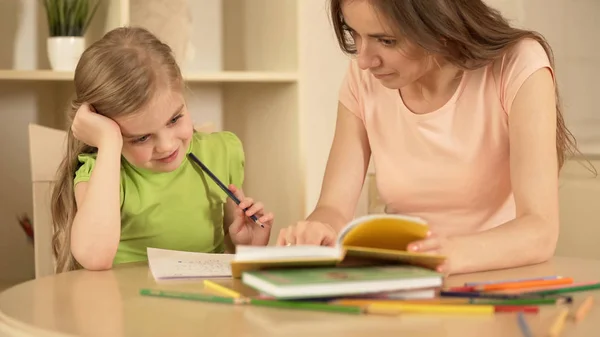 Mother helping daughter with homework, happy smart girl enjoying home education — Stock Photo, Image