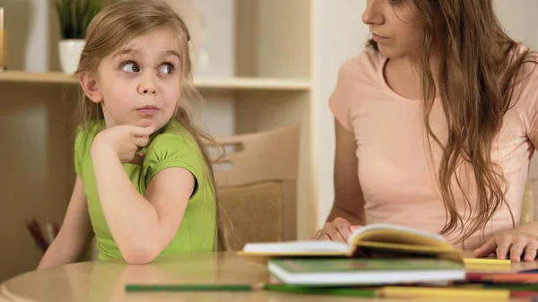 Hija aburrida sorprendentemente mirando a la madre haciéndola hacer la tarea —  Fotos de Stock