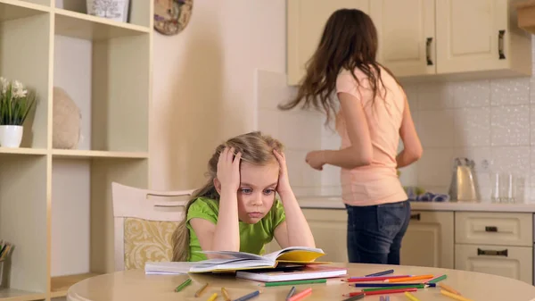 Жінка займається домашніми обов'язками, поки її дочка робить нудне домашнє завдання — стокове фото