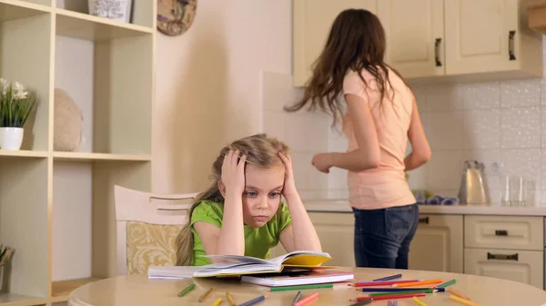 Vrouw houdt zich bezig met huishoudelijke taken terwijl haar dochter saai huiswerk — Stockfoto