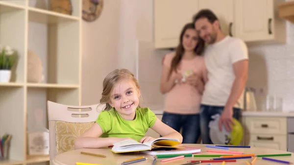 Gelukkig meisje lachend voor camera, liefdevolle ouders knuffelen en dochter te kijken — Stockfoto