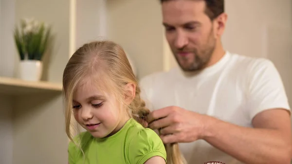 Щасливий батько плете дочки волосся, піклуючись про кохану маленьку дівчинку — стокове фото