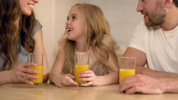 Счастливая здоровая семья пьет апельсиновый сок с улыбками на лицах, утро дома — стоковое фото