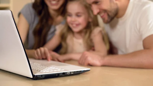 Щасливі батьки і дочка дивляться на ноутбук, дівчина насолоджується дистанційною освітою — стокове фото