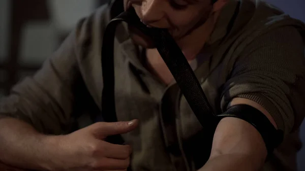 Male junkie holding tourniquet with his teeth, preparing for drug injection — Stock Photo, Image