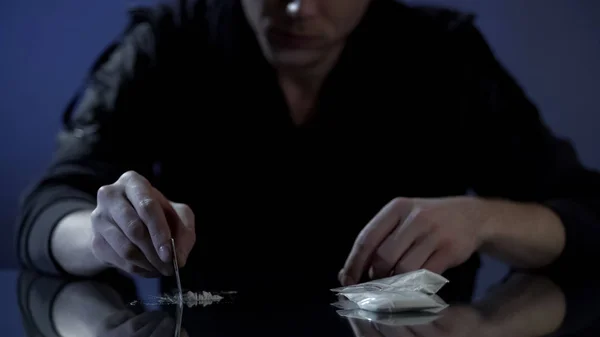 Young wealthy man forms cocaine lines on table, drug addiction among the rich