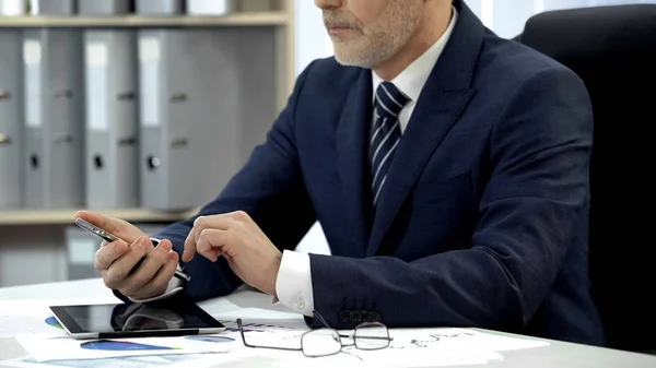 Человек в деловом костюме проверяет электронную почту на смартфоне в офисе, современные технологии — стоковое фото