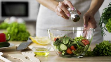 Woman adding salt in vegetable salad glass bowl, health care, excessive salting clipart