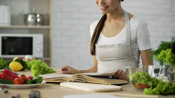 Asian female reading ingredients list for salad in cooking book at home kitchen — Stock Photo, Image