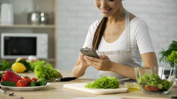 Hymyilevä aasialainen tyttö katsomassa video resepti älypuhelimella ennen ruoanlaittoa illallinen — kuvapankkivalokuva