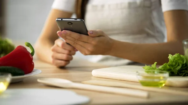 Lähikuva naisten kädet vieritys älypuhelimeen, nainen valitsemalla salaatti resepti — kuvapankkivalokuva