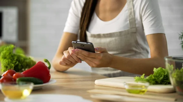 Женщина выбирает салат рецепт на смартфоне на кухне, кулинарное приложение — стоковое фото