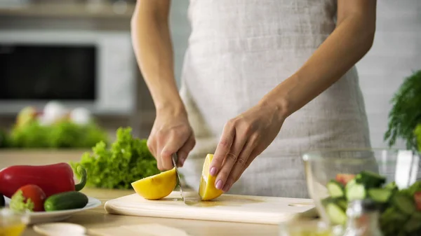 Las manos de mujer joven cortando limón amarillo en el tablero de la cocina en casa, comer sano —  Fotos de Stock