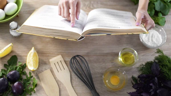 Lady läsning pizza recept i kulinariska bok hemma med köksutrustning på bord — Stockfoto