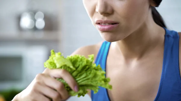 Young lady looking with disgust at green lettuce salad leaves during strong diet — Stock Photo, Image