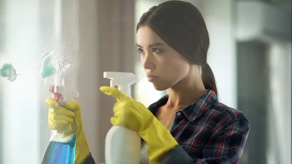 Jonge huisvrouw in handschoenen spuiten schoonmaak vloeistof glasoppervlak, bezetting — Stockfoto