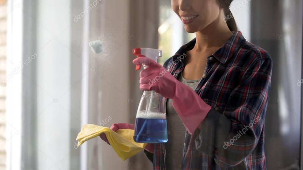 Girl from cleaning service applying cleansing agents to dusty glass surfaces