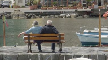 Ischia, İtalya - Temmuz 2014 yaklaşık: İnsanlar adada. Bankta oturan ve yerleşik tekneler ile defne üzerinde manzarayı yaşlı çift