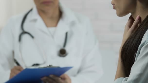 Mujer asiática joven diciendo síntomas, médico escuchando y manteniendo registros médicos — Vídeo de stock