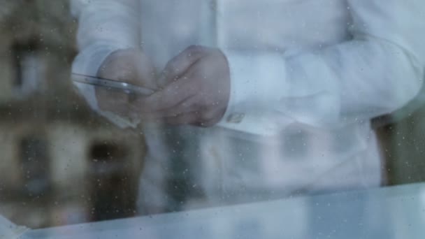 Depressed divorced man texting from smartphone, rain dropping on window glass — Stock Video