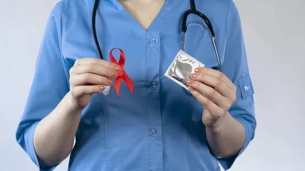 Ginecologista segurando fita vermelha e preservativo, conscientização da AIDS, advertência sobre IST — Fotografia de Stock