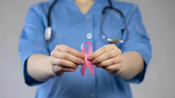 Trabajadora médica de uniforme azul con cinta rosa en las manos, riesgo de cáncer de mama — Foto de Stock