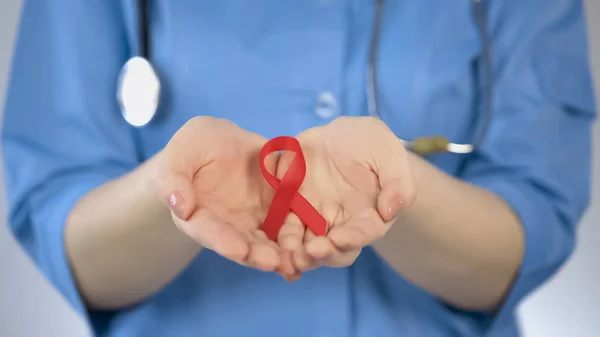 Ginecóloga femenina con abrigo azul sosteniendo cinta roja en las palmas de las manos, conciencia del SIDA — Foto de Stock