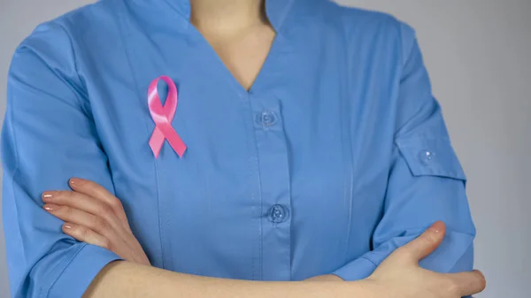 Médico femenino con cinta rosa en uniforme azul, conciencia de cáncer de mama — Foto de Stock