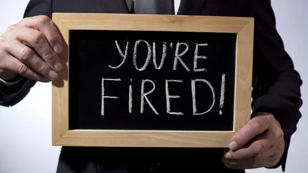 Você está demitido com exclamação escrita em quadro negro, empresário segurando sinal — Fotografia de Stock