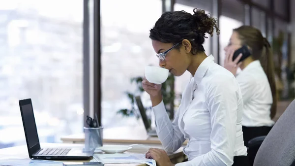 Aantrekkelijke vrouwelijke beambte drinken koffie en het lezen van grafieken — Stockfoto