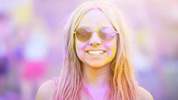 Smiling girl in sunglasses covered in colorful dyes, summer vacation, youth