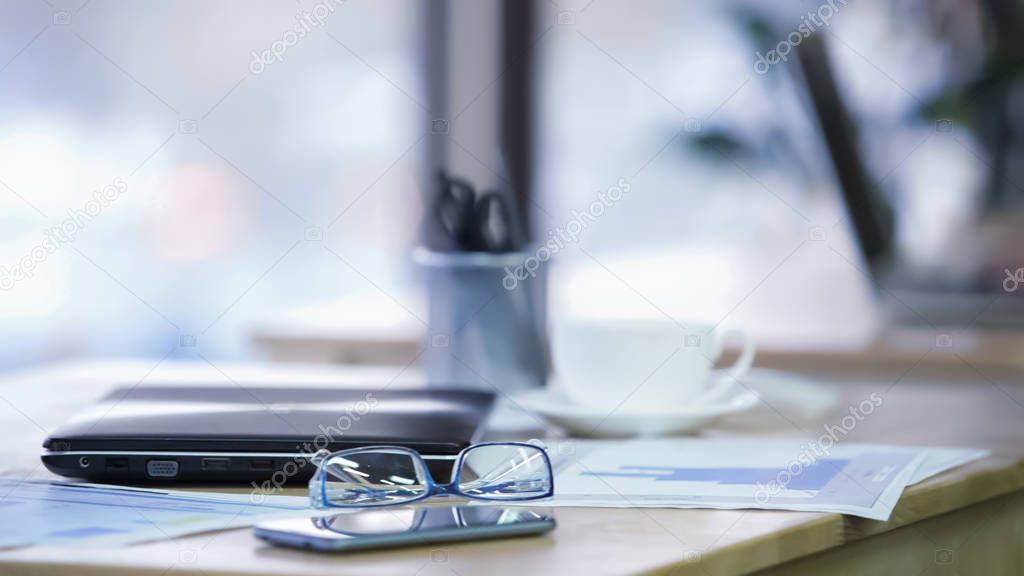Workplace in office, eyeglasses, smartphone and closed laptop lying on table