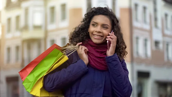 Kvinna med shoppingkassar ringa kvinnliga vänner att berätta om rabatter i butiker — Stockfoto