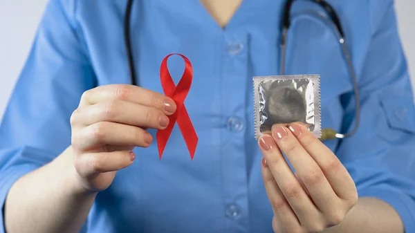 Kırmızı kurdele prezervatif, cinsel yolla bulaşan hastalıklar uyarı, holding doktor AIDS — Stok fotoğraf