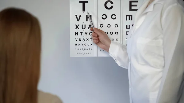 Médico ocular verificando a visão de paciente do sexo feminino mostrando letras, oftalmologista — Fotografia de Stock